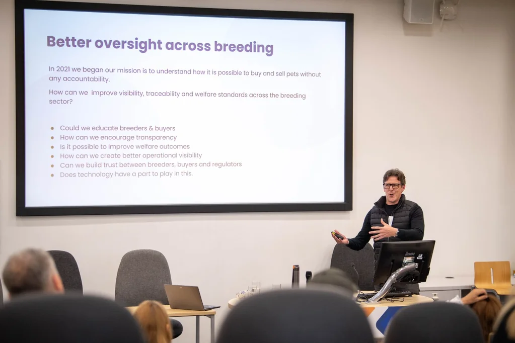 A speaker presenting to an audience about oversight and traceability in dog breeding